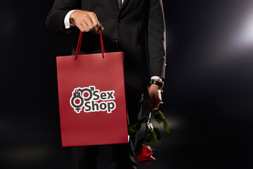 Charming young man holding a red shopping bag and a single rose in a dramatic setting