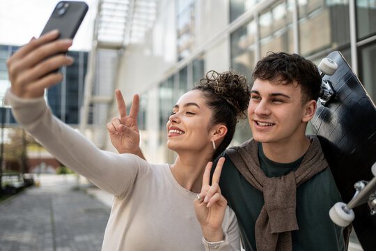 Young students taking a selfie with skateboard and peace sign - Powered by Adobe