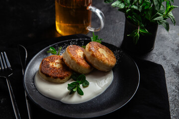 Cheesecakes with cream sauce and mint in a black plate on the table. Breakfast