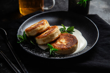 Cheesecakes with cream sauce and mint in a black plate on the table. Breakfast