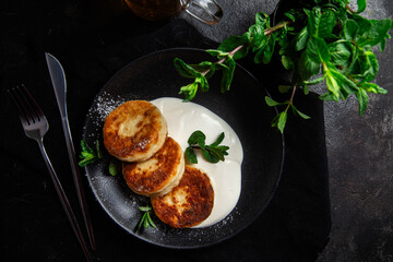 Cheesecakes with cream sauce and mint in a black plate on the table. Breakfast