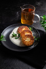 Cheesecakes with cream sauce and mint in a black plate on the table. Breakfast