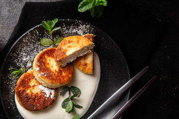 Cheesecakes with cream sauce and mint in a black plate on the table. Breakfast
