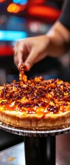 A hand garnishes a savory, cheesy pizza with sauce and toppings in a vibrant restaurant setting.