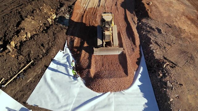High angle top down late afternoon footage of bulldozer maching covering layers of geotextile with dirt and soil for the construction of a highway. Freeway build site with geosynthetic fabric burried

