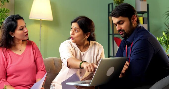 Senior Indian mother and young daughter discussing plans with male architect, realtor or financial advisor in formal attire showing design or loan options on laptop during client consultation meeting