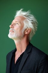 Fototapeta premium Concept art idea design of style for aging men. Elegant men's shoulder-length taper haircut - midlife white man with white hair. A happy man in a studio photo. Green solid background.