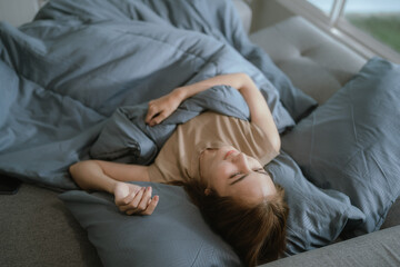 Attractive young woman stretching happily on a cozy bed in a sunlit bedroom, enjoying a peaceful and relaxing morning moment.