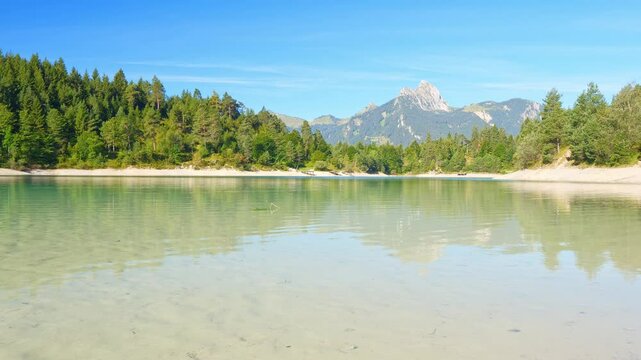 Peaceful alpine lake Urisee with turquoise waters reflecting mountain forests and sky near Reutte in the Tyrolean highlands