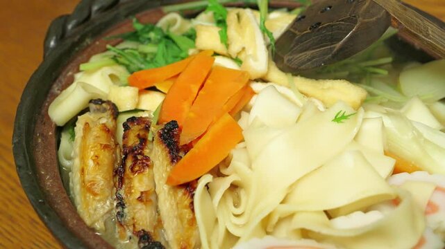 Nagoya's specialty, Kishimen noodle stew in miso broth, Japanese style noodles, deep-fried tofu, carrots, chicken, and Naruto