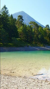 Turquoise glacial lake Urisee in a peaceful alpine valley near Reutte, surrounded by green woods and rocky highland slopes