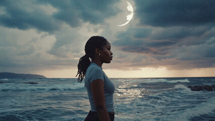 A lone woman stands on the beach, lost in thought as she gazes up at the moon