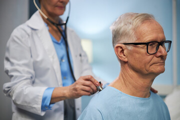 Elderly Caucasian man having his heartbeat checked by medical professional wearing lab coat and...