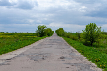 A patched and recently repaired asphalt road in the countryside leading uphill. The empty road stretches through a quiet rural area, symbolizing solitude, infrastructure, and simple everyday life.