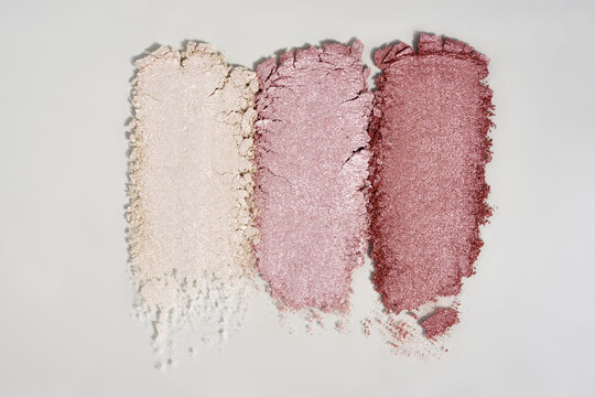Swatches of crushed shimmer eyeshadows or highlighters arranged horizontally on a light gray background.