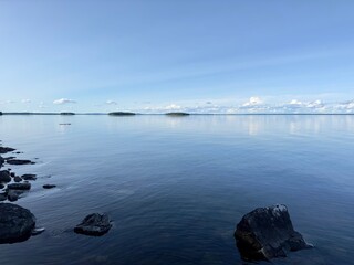 Calm lake scene, with reflections on the water, small islands, and a bright blue sky in Sweden.