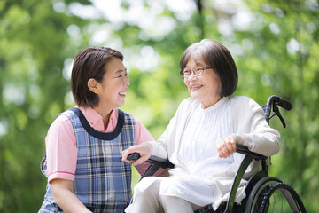 A caregiver and an elderly person look at each other and smile as they stroll through the greenery.