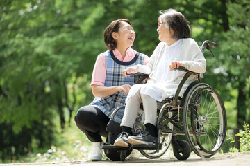 緑の中散歩をする介護士と高齢者の見つめ合う笑顔の全身