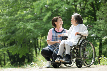 緑の中散歩をする介護士と高齢者の見つめ合う笑顔の全身