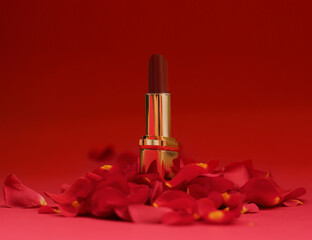 Luxury red lipstick surrounded by rose petals on red background. Glamorous beauty concept for cosmetics, makeup products, and feminine elegance.