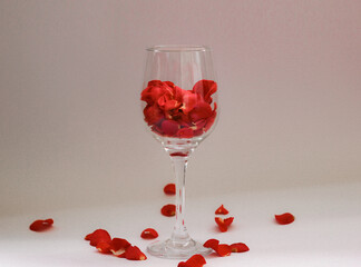 Romantic still life with red rose petals in a wine glass on soft pink background. Perfect for Valentine’s Day, love-themed content, or elegant floral compositions.