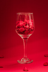 A wine glass filled with red rose petals stands on a vivid red background. A bold, romantic still life perfect for Valentine's Day, love-themed visuals, or floral minimalism.