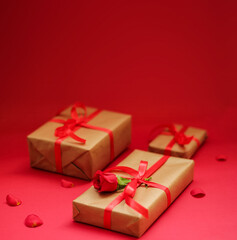 Elegant gift boxes wrapped in kraft paper with red ribbons and a red rose on a vibrant red background, perfect for romantic celebrations and special occasions.