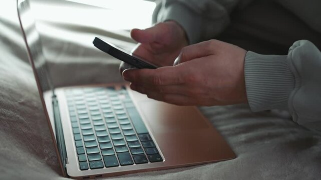 A man flips through social media on his phone in the background of an open laptop