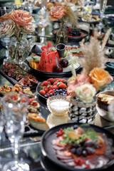 Gourmet spread features an assortment of fresh fruits, including strawberries and blueberries, alongside savory appetizers with smoked salmon and roast beef on a glass table.
