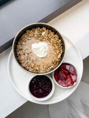 Oatmeal with Muesli, Yogurt, and Pumpkin Seeds Served with Blueberry Jam and Stewed Plums. Modern Breakfast Concept. Handmade Mobile Photo, Not AI