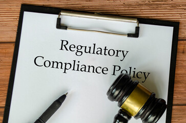 Regulatory Compliance Policy text on clipboard surrounding with magnifying glass and gavel....