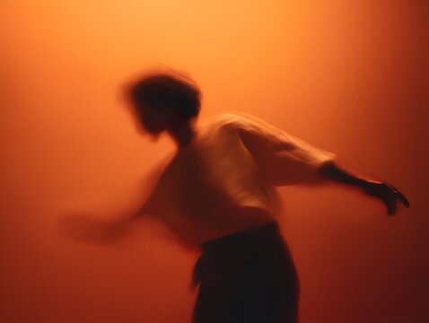 A dynamic silhouette of a person in motion against a vivid orange backdrop creating an artistic and abstract visual experience