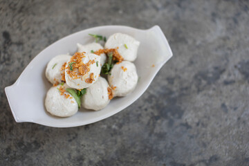 Baked pork meatballs in a white plate on a cement tabletop.