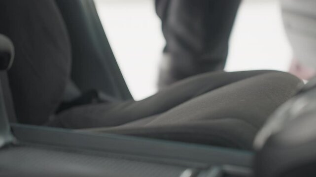 close up interior view of car seat with open door as person enters and sits down, daylight visible through open doorway, fabric seat texture clearly seen