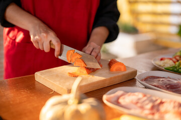 A woman is cutting carrots on a wooden cutting board