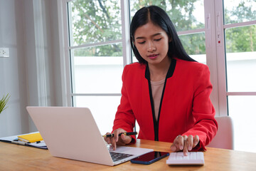 Asian businesswoman working in a modern office, focused on a task at hand. Amidst technology and paperwork, she exudes confidence, professionalism, and commitment in a corporate environment.