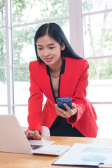 Obraz premium Asian businesswoman working in a modern office, focused on a task at hand. Amidst technology and paperwork, she exudes confidence, professionalism, and commitment in a corporate environment.