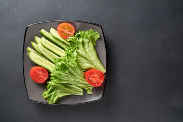 On a plate are sliced ​​cucumbers, tomatoes and cabbage. On a dark background. Low key.