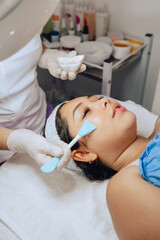 Naklejka premium Photo of a young Colombian mestiza girl in a beauty spa where she is having a facial cleansing and is going through the step of applying a moisturizing gel on her face.