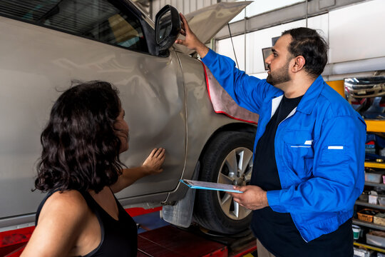 Caucasian male auto mechanic showing and explaining female customer in auto repair shop
