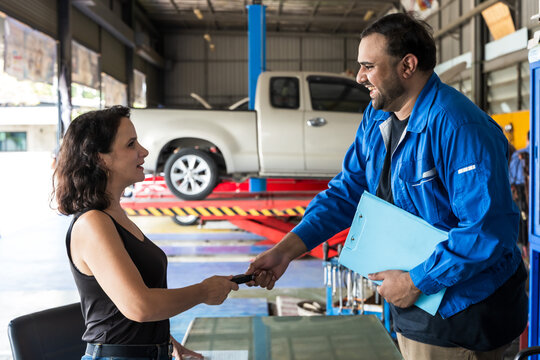 Caucasian male auto mechanic giving car key to female customer in auto repair shop - Powered by Adobe