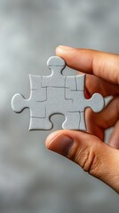 Hand holding a single white puzzle piece against a blurred background, highlighting concentration and creativity