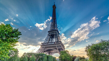 The Eiffel tower with warm rays of light in clouds during sunset timelapse hyperlapse.