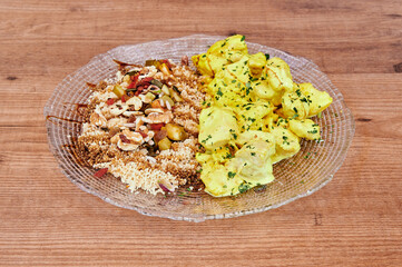 A plate of food with a side of potatoes. The plate is on a wooden table. The food on the plate includes rice, potatoes, and chicken