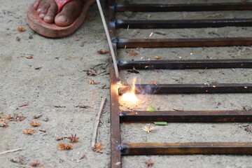 Barefooted Man Welding Metal Grid with Sparks Outdoors Industrial Construction