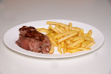 A plate of steak and french fries. The steak is brown and the fries are golden. The plate is white