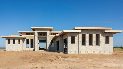 Concrete shell of an upscale single-family house under construction by an artificial lake in a suburban residential development on a sunny morning in southwest Florida