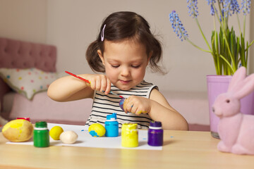 Little child girl paint Easter eggs at home. kid is preparing for Easter.