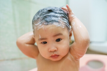 Child enjoying a playful bath, washing hair with shampoo in a bright bathroom setting