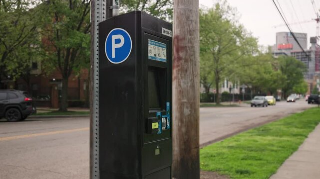Pay here parking meter sign and station for car drivers to add payment for time spent parked in city public park area along sidewalk and road near downtown Columbus, Ohio in United States